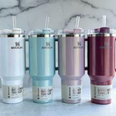 four different colored tumblers lined up next to each other on a marble countertop