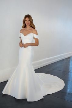 a woman in a white wedding dress standing next to a wall and posing for the camera