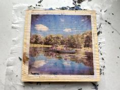 an altered photograph of a lake with trees and clouds in the background on a piece of wood