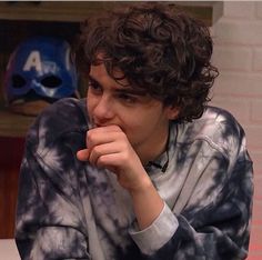 a young man sitting at a table with his hand on his chin and looking off to the side