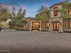 a large house with many windows and trees in the front yard at dusk, surrounded by brick pavers