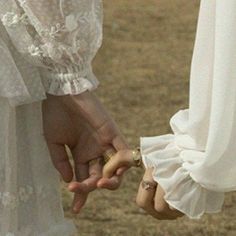 two people are holding hands and touching each other's fingers in an open field