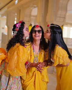 three women dressed in bright yellow clothing and flower crowns are kissing each other with their mouths open