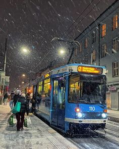 a blue and white bus driving down a snow covered street next to people walking on the sidewalk