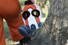 a woman is holding a knitted mitt in front of a tree