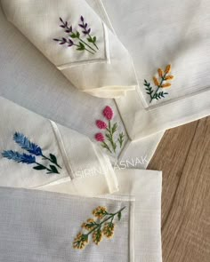 four embroidered napkins with flowers on them sitting on a wooden table next to each other