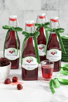 four bottles of cherry jam next to a bowl of cherries and plates with green ribbons