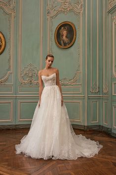 a woman in a white wedding dress standing in front of a wall with portraits on it