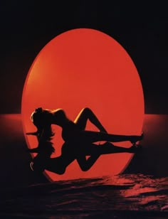 the silhouette of a woman in front of a large orange ball with her legs spread out