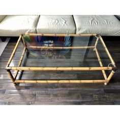 a glass and bamboo coffee table on top of a hard wood floor with a couch in the background