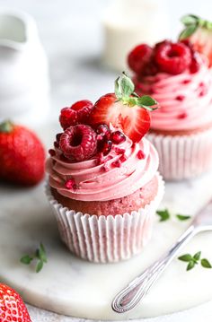 two cupcakes with raspberry frosting and fresh strawberries on top