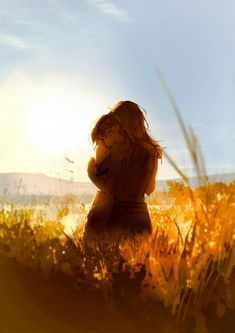 a person sitting in the grass with their back to the camera and looking at the sun