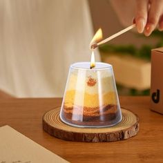 a person lighting a candle in a glass on top of a wooden table next to a box