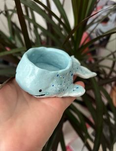 a hand holding a blue ceramic whale planter in front of a potted plant