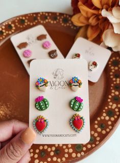 a pair of earrings with cactus designs on them sitting on a plate next to flowers