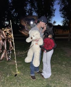 a couple kissing in front of balloons and a teddy bear on the grass at night