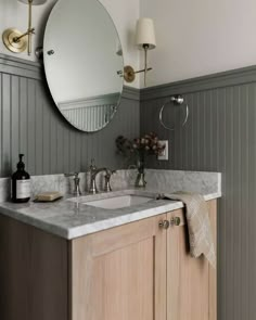 a bathroom vanity with two sinks and a large round mirror above it, in front of a gray striped wall