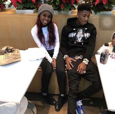 two young people sitting at a table in front of some potted plants and flowers