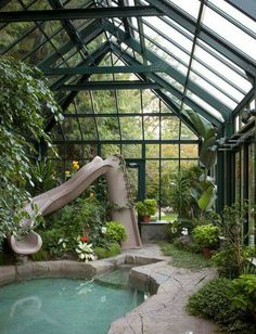 an indoor swimming pool with a slide in the center and plants around it, surrounded by greenery