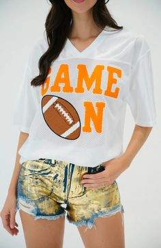 a young woman wearing shorts and a football t - shirt with the name game on