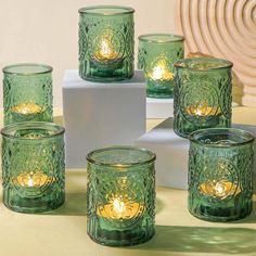 six green glass candles sitting on top of a table