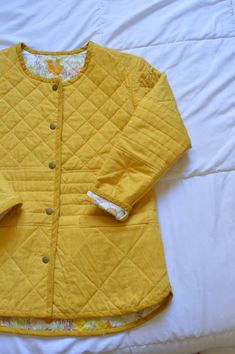 a yellow quilted jacket laying on top of a white bed next to a pillow