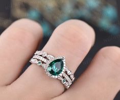 a woman's hand holding a ring with an oval shaped green stone in the center