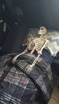 a skeleton sitting on top of a bed next to pillows