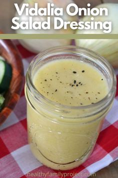 a mason jar filled with dressing next to cucumbers and onions on a checkered tablecloth