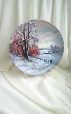 a plate with a painting of a snowy scene on the front and side, sitting on a white cloth