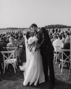 a bride and groom kissing in front of an outdoor wedding ceremony with rows of chairs