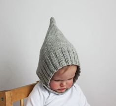 a baby wearing a knitted hat sitting in a wooden chair