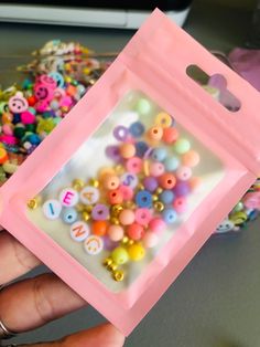 a hand holding a pink plastic bag filled with lots of different colored beads and buttons