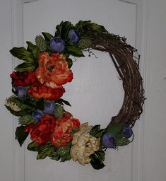 a wreath is hanging on the front door with red, orange and blue flowers in it