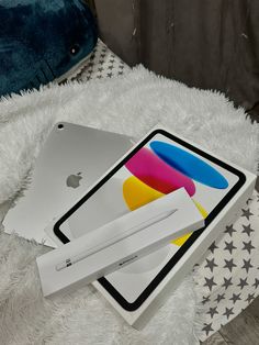 an apple laptop and pen sitting on top of a white fluffy blanket next to each other