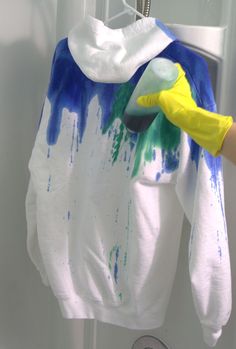 a person wearing yellow rubber gloves is painting a white shirt with blue and green paint