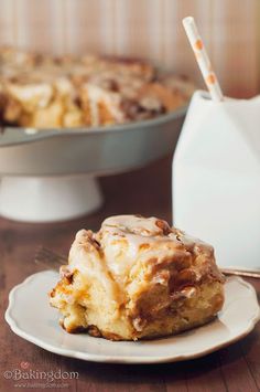 a piece of cinnamon roll sitting on top of a white plate next to a cake dish