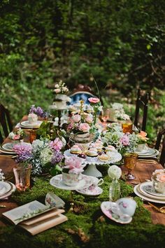 a table with plates, cups and saucers on it in the middle of a forest