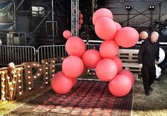 a man walking past a bunch of pink balloons on top of a wooden bench in front of a stage