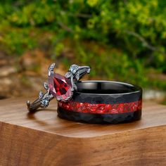 two wedding rings with red and black bands on top of a wooden table in front of some bushes