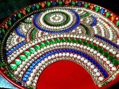 a red plate with green, blue and white designs on the top is sitting on a table