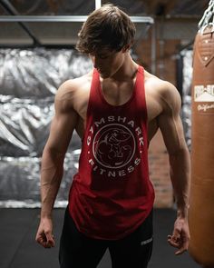 a man standing next to a punching bag wearing a red tank top with the words smash fitness printed on it