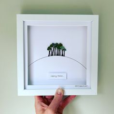 a hand holding up a white frame with three trees on it