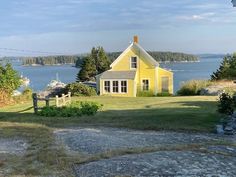 a small yellow house sitting on top of a lush green field next to the ocean