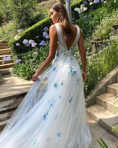 a woman wearing a white dress with blue flowers on the skirt is walking down some steps