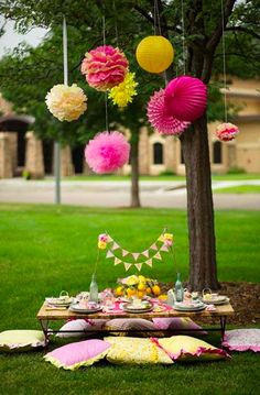 a picnic table with pink, yellow and white paper lanterns hanging from it's branches