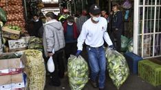 people are walking through an open market with bags of produce in front of the store