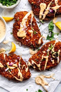 several crab cakes with sauce and lemon wedges on a piece of paper next to some dipping sauce