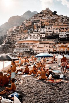 a group of people sitting on top of a sandy beach next to the ocean with buildings in the background