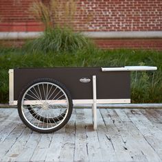 an old fashioned bike is sitting on a wooden deck outside in front of a brick building